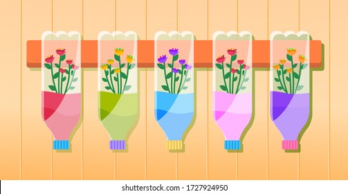Multi-colored flowers in bottles hang on a wooden plank on the wall. Reuse plastic bottle as flower pots in home garden and craft recycle theme. Growing decorative flower in a plastic bottle for water