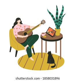 Music online learning, education. Guitar lessons. Young woman sitting home and training to play the guitar with tablet watching video lesson. 
