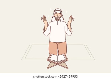 Muslim man prays on knees in front of koran, observing islamic ritual during holy month of ramadan. Guy in arabic cape visiting mosque in ramadan to turn to allah or prophet muhammad