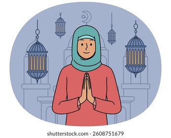 Muslim woman in hijab makes prayer gesture standing near mosque and traditional islamic lanterns. Girl visits mosque during holy month of ramadan and wants to pray to allah or prophet muhammad
