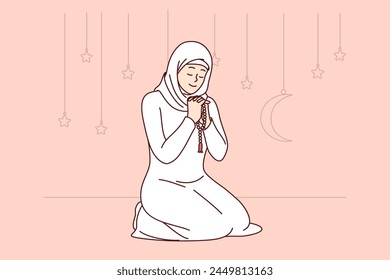 Muslim woman honors holy month of ramadan, reading prayer sitting on knees, wearing islamic or arabic traditional clothing. Praying girl smiles, celebrating onset of ramadan and thanks allah