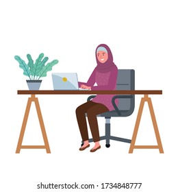 A muslim woman is smiling with in front of her laptop in her working desk