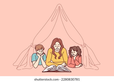 Nanny and two small children reading book lying on floor in tent enjoying fairy tale story. Mom spends time with pre-adolescent children and gets positive emotions from self-parenting