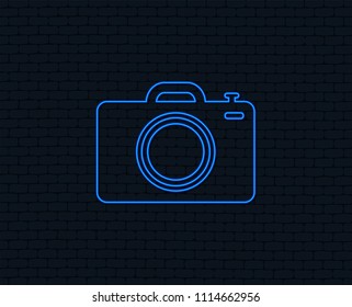 Neon light. Photo camera sign icon. Digital photo camera symbol. Glowing graphic design. Brick wall. Vector