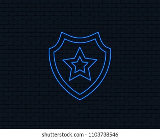 Neon light. Shield with star icon. Favorite protection symbol. Glowing graphic design. Brick wall. Vector
