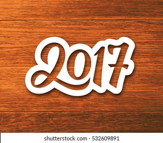 New Year 2017 paper label with calligraphic number on wood background. Vector greeting card design template for winter holidays