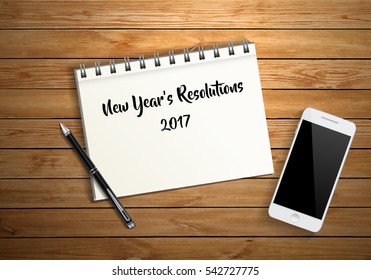 New year's resolutions word on blank notebook paper, pen and smart phone on wood background, financial concept, business strategy