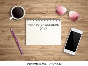 New year's resolutions word on blank notebook paper coffee, sunglasses,pen and smart phone on wood background, financial concept, business strategy