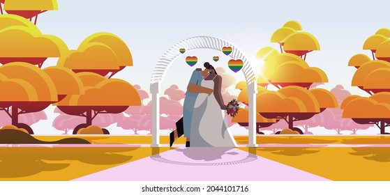 newlywed lesbian couple with flowers kissing near wedding arch transgender love LGBT community wedding celebration