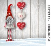 Nisser in Norway and Denmark, Tomtar in Sweden or Tonttu in Finnish, Scandinavian folklore elves, nordic christmas motif, Tomte standing in front of gray wooden wall in snow, with red decorated hearts.