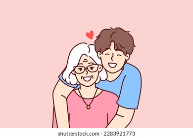 Noble guy teenager hugging elderly grandmother showing love and care for ancestors and communicating with family. Happy retired woman near caring son spending time in family atmosphere 