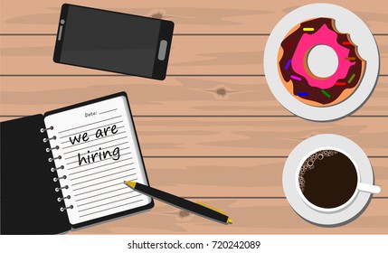 Notebook on wooden table with coffee and donut with word we are hiring