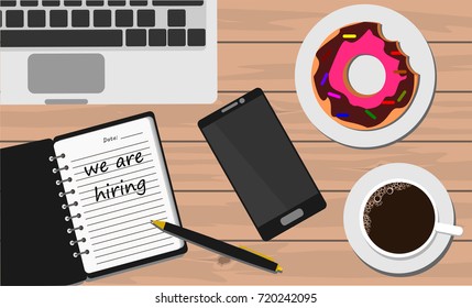 Notebook on wooden table with coffee and donut with word we are hiring