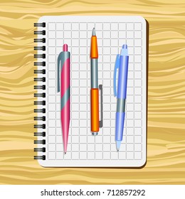 Notebook,  red  pen, orange pen and blue pen on a wooden table