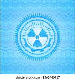 nuclear, radioactive icon inside light blue water wave emblem.
