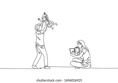 One single line drawing of young mother sitting on floor and reading book to son while father playing with daughter vector illustration. Happy family parenting concept. Continuous line draw design
