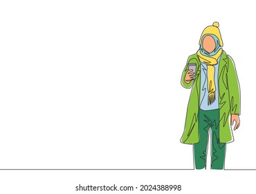 One single line drawing of young attractive happy muslimah wear beanie hat and hold coffee cup. Beauty Asian woman model in trendy hijab fashion concept continuous line draw design vector illustration