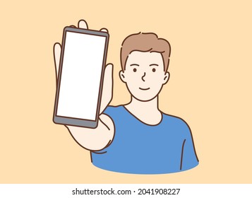 Online communication, smartphone screen. Young smiling man showing smartphone screen with white mockup for text or lettering.