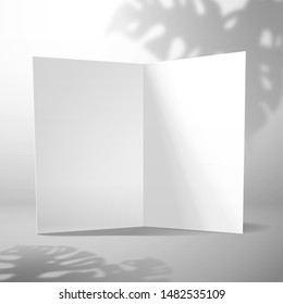 An open blank card stands against a white wall with the shadow of a Monstera plant. Mockup for design