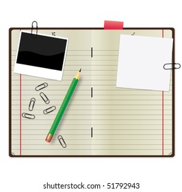 Open copybook with a green pencil, photograph and paper clips.