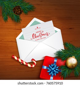 Open envelope with card Merry Christmas and Happy New Year with fir tree branches, gold bubble, candy cane, box gift and blue bow on wooden background. Vector calligraphy lettering