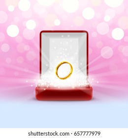 Open jewelry box with gold wedding ring, glowing from inside on abstract bokeh background. Engagement gift