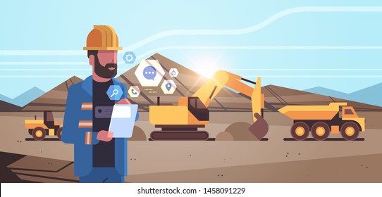 open pit man worker in helmet using mobile app excavator loading soil on dump truck professional equipment working on coal mine production opencast stone quarry background portrait horizontal