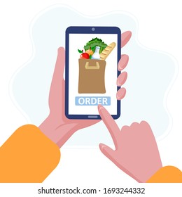 Order grocery online with smartphone from home. Hand press the button to order fresh, organic food and drink for fast delivery from market. Shopping bag full of vegetables, fruits and bread.