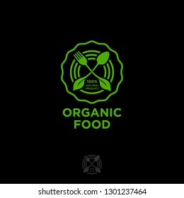 Organic food logo. Green food emblem. Green leaves, fork and spoon in a circle isolated on a dark background. Nature health meal, vegetarians emblem.