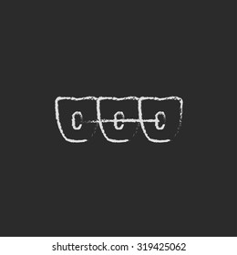 Orthodontic braces hand drawn in chalk on a blackboard vector white icon isolated on a black background.