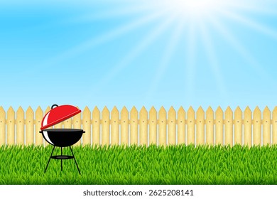 Outdoor charcoal barbecue grill with open lid standing on green grass near wooden fence on a bright sunny day