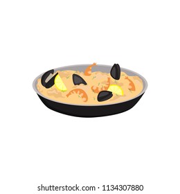 Paella with shrimps, oysters and slices of lemon in black pan. Traditional Spanish dish.