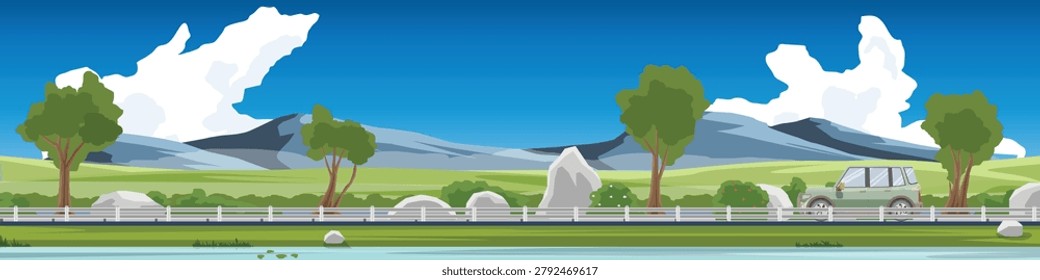 Panoramic horizontal banner of green car driving on asphalt road.Green fields trees and large grey mountains under a bright blue sky. Grassy hills and a stream flowing along the side of the road.