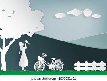 Paper art vector illustration of girl with bird and bicycle, tree, wooden fence, cloud , sun, mountain on sky background.