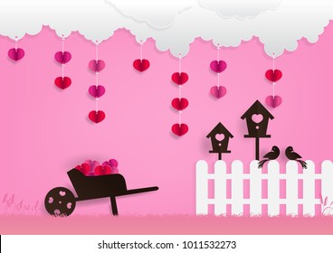 Paper art vector illustration of wheelbarrow, birdhouses, white fence, couple birds, heart ornaments, white clouds on pink background for Valentine's day festival decoration. 