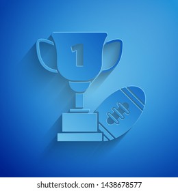 Paper cut Award cup and American football ball icon isolated on blue background. Winner trophy symbol. Championship or competition trophy. Paper art style. Vector Illustration