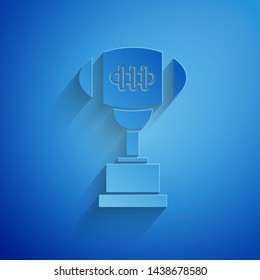 Paper cut Award cup and American football ball icon isolated on blue background. Winner trophy symbol. Championship or competition trophy. Paper art style. Vector Illustration