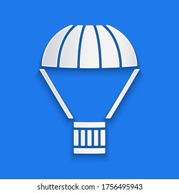 Paper cut Box flying on parachute icon isolated on blue background. Parcel with parachute for shipping. Delivery service, air shipping. Paper art style. Vector Illustration
