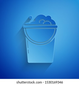 Paper cut Bucket with foam and bubbles icon isolated on blue background. Cleaning service concept. Paper art style. Vector Illustration