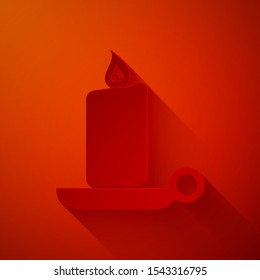 Paper cut Burning candle in candlestick icon isolated on red background. Old fashioned lit candle. Cylindrical candle stick with burning flame. Paper art style. Vector Illustration