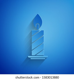 Paper cut Burning candle in candlestick icon isolated on blue background. Cylindrical candle stick with burning flame. Paper art style. Vector Illustration