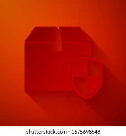 Paper cut Delivery pack security symbol with shield icon isolated on red background. Delivery insurance. Insured cardboard boxes beyond the shield. Paper art style. Vector Illustration