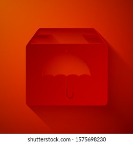 Paper cut Delivery package with umbrella symbol icon isolated on red background. Parcel cardboard box with umbrella sign. Logistic and delivery. Paper art style. Vector Illustration