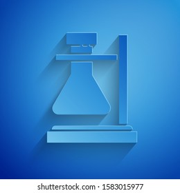 Paper cut Glass test tube flask on stand icon isolated on blue background. Laboratory equipment. Paper art style. Vector Illustration