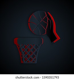 Paper cut Hand with basketball ball and basket icon isolated on black background. Ball in basketball hoop. Paper art style. Vector Illustration