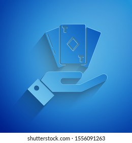 Paper cut Hand holding deck of playing cards icon isolated on blue background. Casino gambling. Paper art style. Vector Illustration