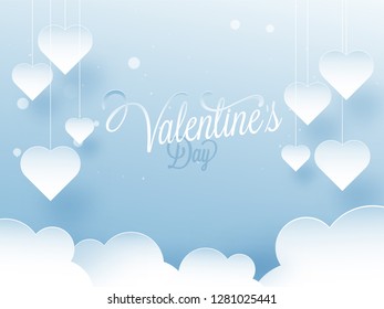 Paper cut heart shapes hanging on blue cloudy background with stylish lettering of Valentine's Day.