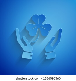Paper cut Human hands holding four leaf clover icon isolated on blue background. Happy Saint Patrick day. Paper art style. Vector Illustration