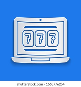 Paper cut Laptop and slot machine with lucky sevens jackpot icon isolated on blue background. Online casino. Paper art style. Vector Illustration