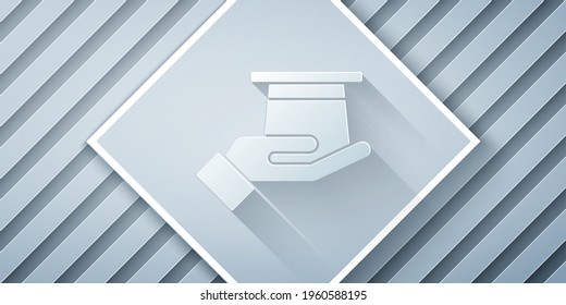 Paper cut Magician hat in hand icon isolated on grey background. Magic trick. Mystery entertainment concept. Paper art style. Vector